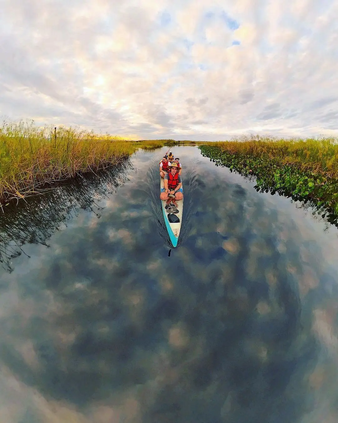 Canoa com quatro pessoas num canal de água escura do Marimbus, refletindo as nuvens