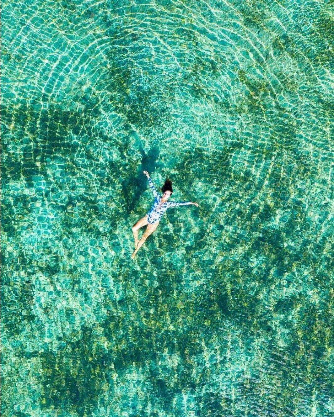 Vista de cima de uma mulher boiando em água turquesa rasa e transparente