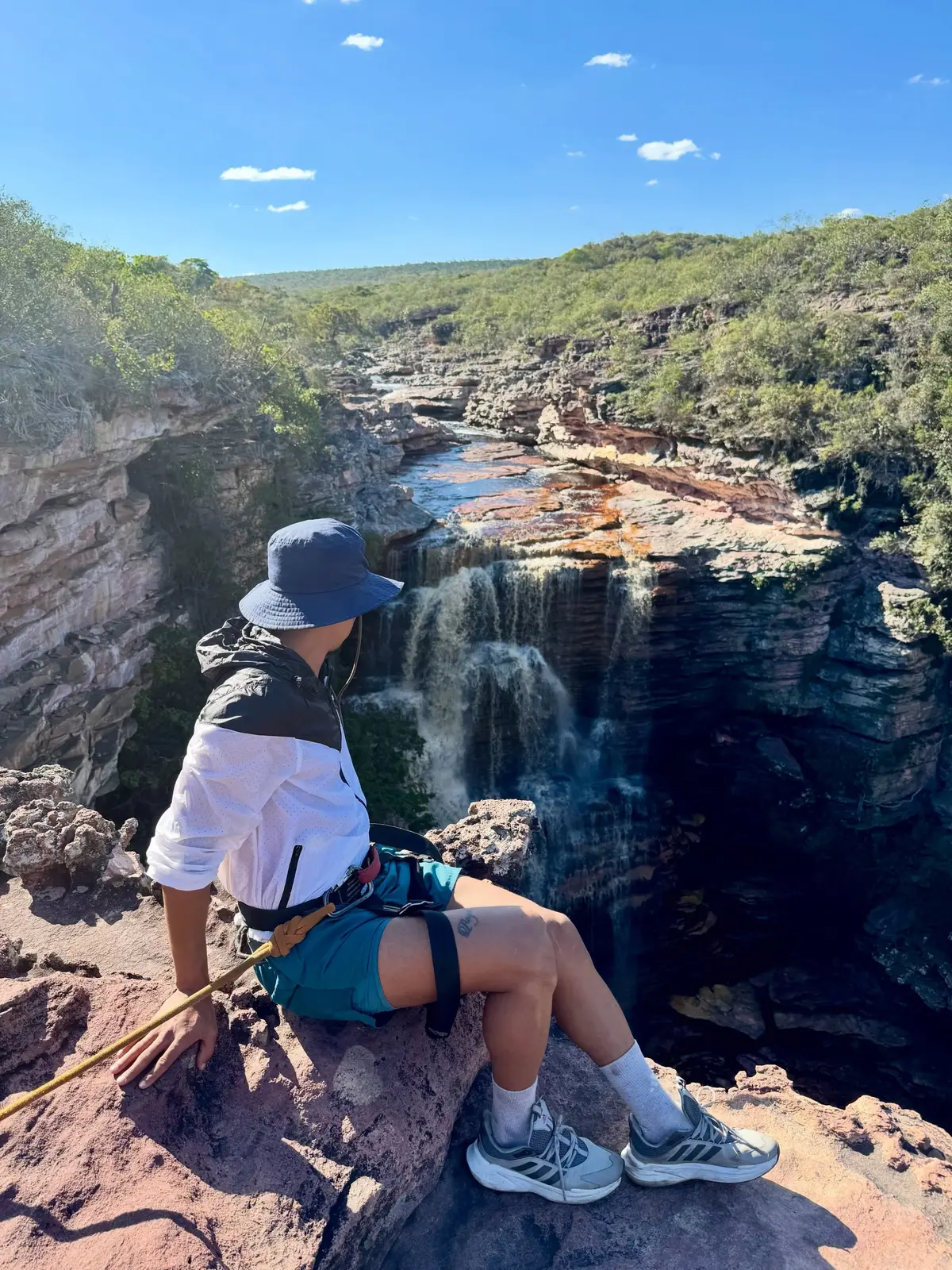Pessoa de cadeirinha e corda sentada na borda de pedra acima da cachoeira do Poço do Diabo