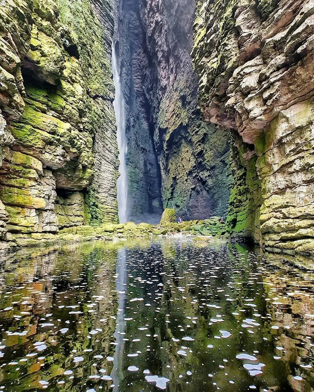 Cachoeira fina caindo no fundo de um cânion estreito, sobre um poço espelhado