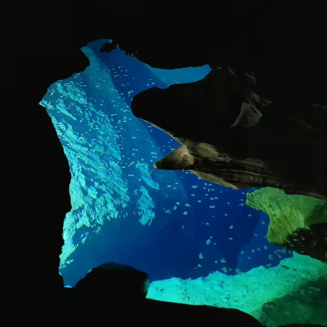 Água azul intensa iluminada pela abertura de uma gruta escura