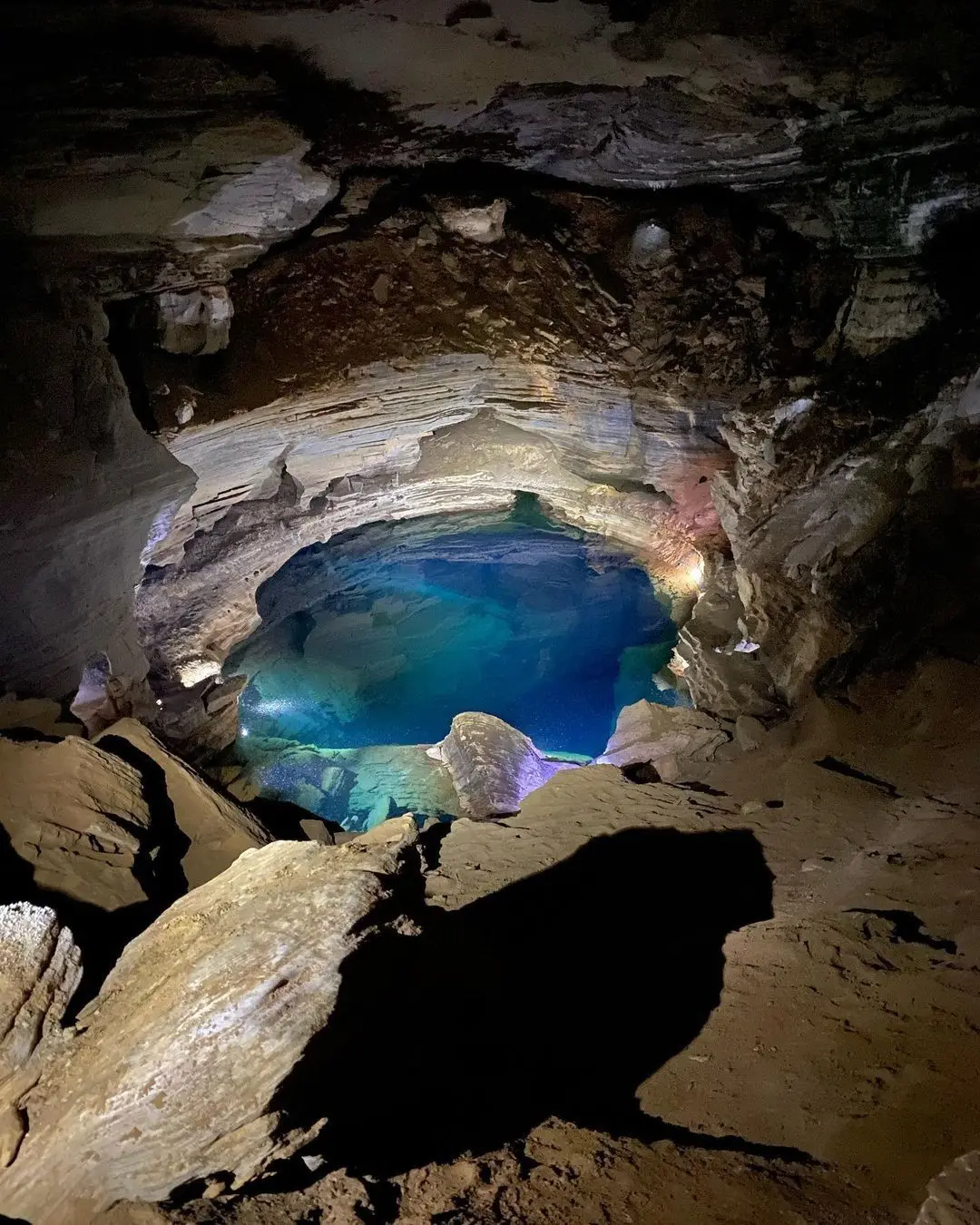 Pequeno poço de água azul dentro de uma gruta escura
