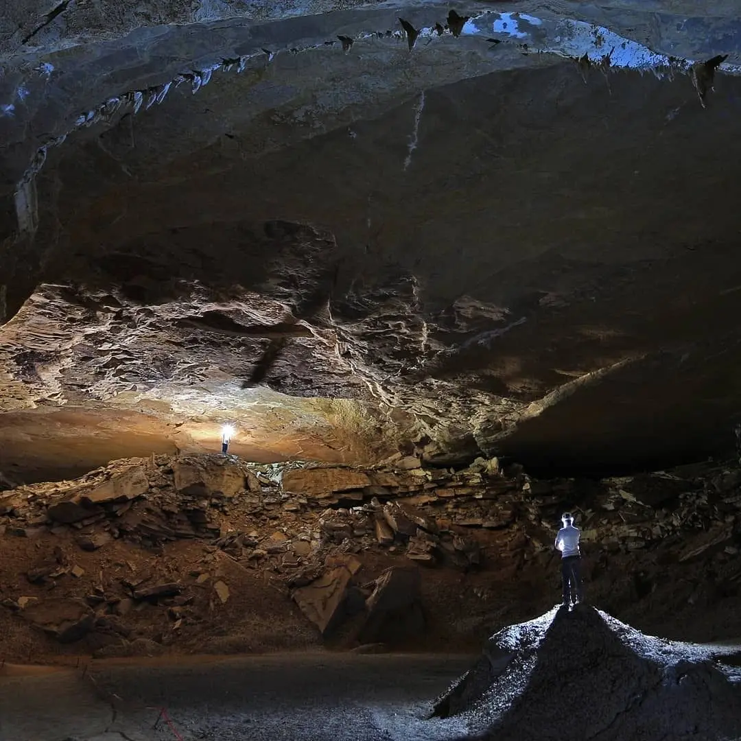 Salão enorme de caverna iluminado pelas lanternas de duas pessoas