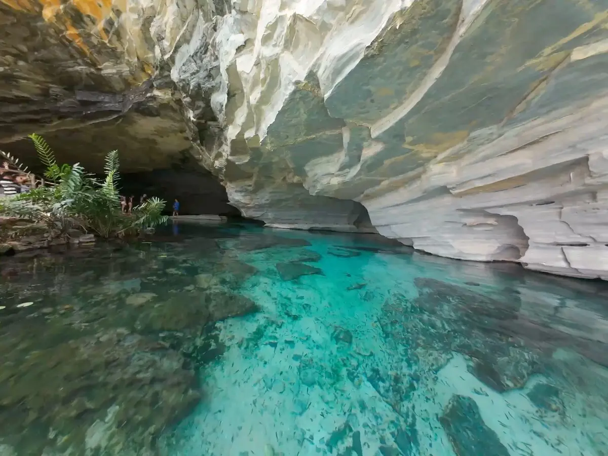 Água azul-turquesa transparente sob o paredão de rocha clara da Gruta da Pratinha