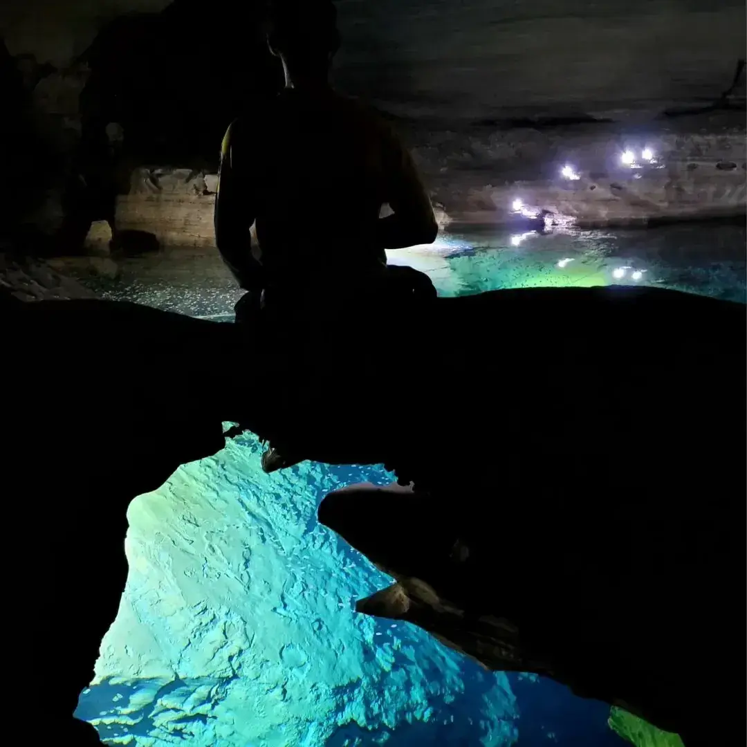 Silhueta de uma pessoa diante da água azul no fundo de uma gruta