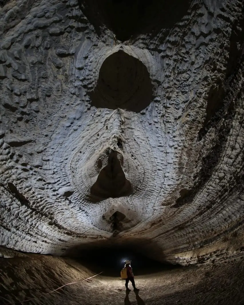 Salão de gruta com o teto esculpido pela água e uma pessoa de capacete
