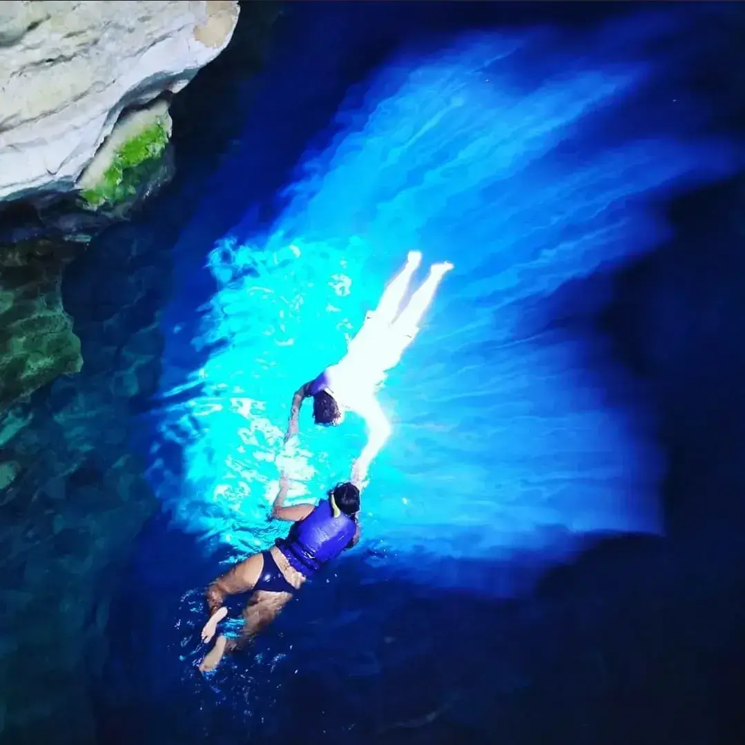 Duas pessoas de colete flutuando dentro do feixe de luz azul do Poço Azul