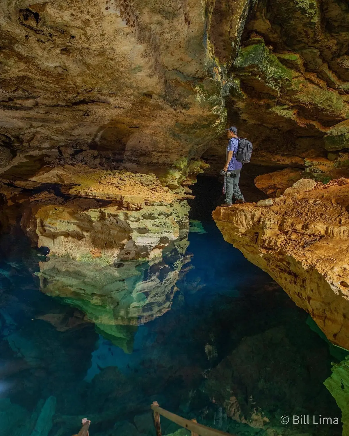 Fotógrafo com câmera numa pedra sobre a água azul iluminada do Poço Azul, dentro da gruta
