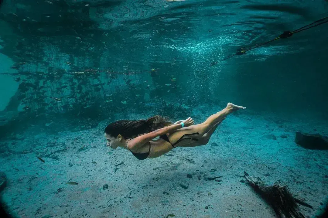 Mulher nadando debaixo d'água entre peixes no Rio Pratinha, ao lado do cabo-guia da flutuação
