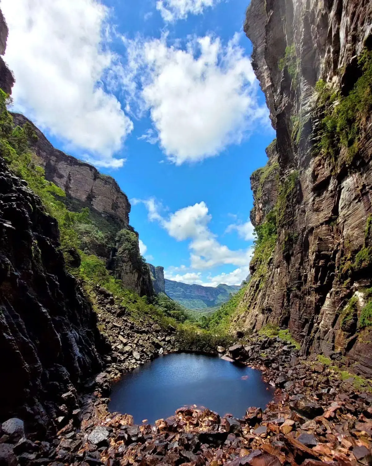 Poço escuro no fundo de um cânion de paredões altos, com o vale e o céu azul ao fundo
