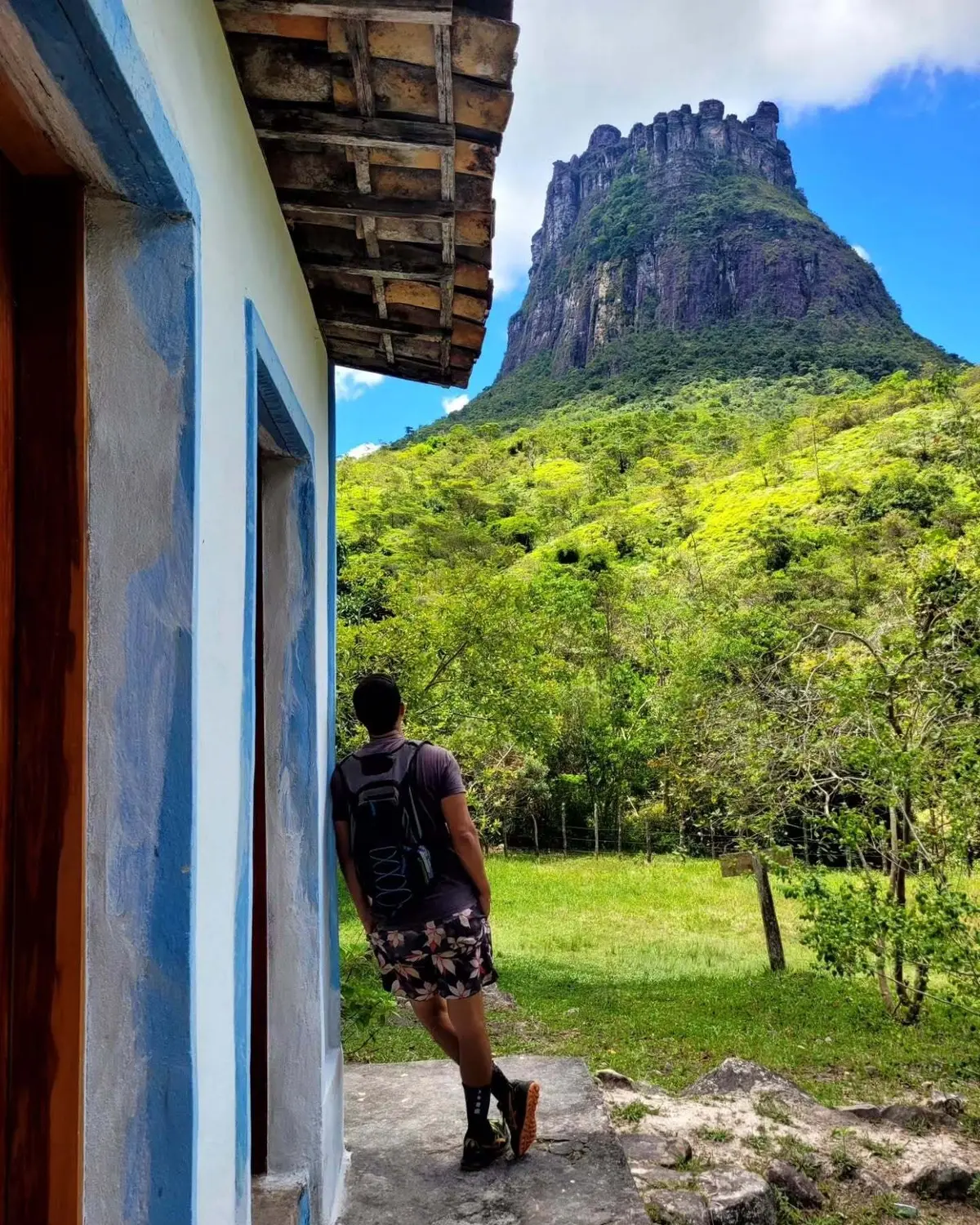 Caminhante encostado numa casa branca e azul, com o Morro do Castelo ao fundo