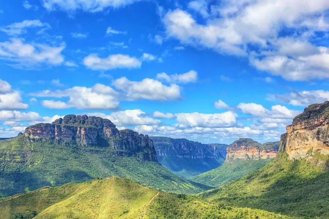 Vale do Pati visto do alto: morros verdes cortados por uma trilha de terra, com paredões de topo plano ao fundo sob céu azul