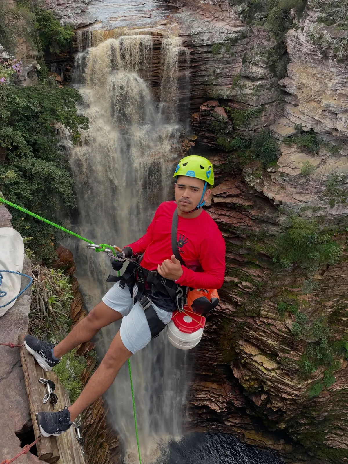 Rapel ao lado da cachoeira do Poço do Diabo: rapaz de capacete verde e camisa vermelha pendurado na corda sobre o cânion