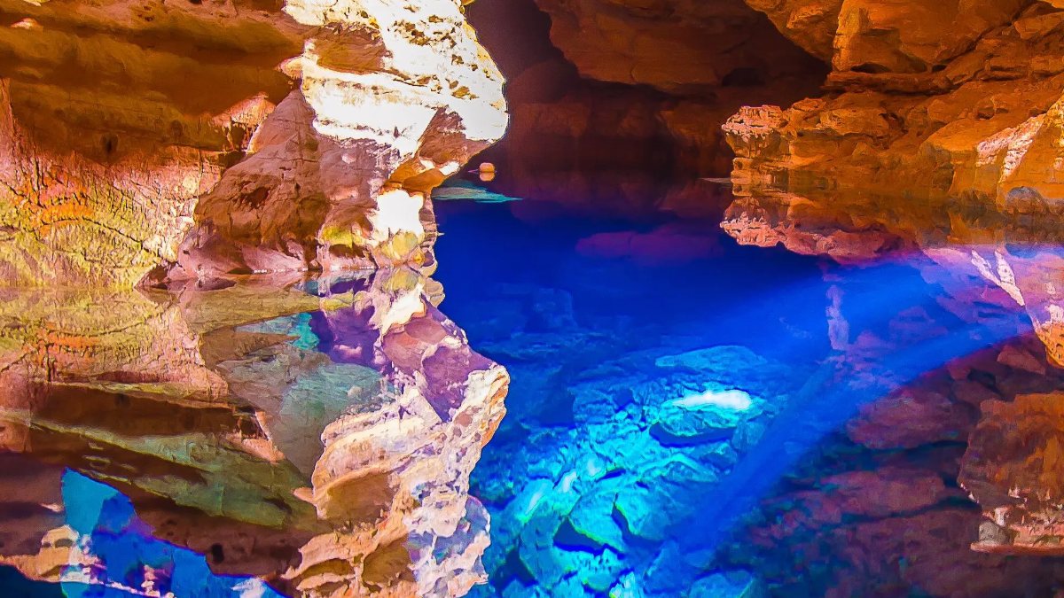 Feixe de luz azul atravessando a água transparente do Poço Encantado, no fundo da caverna